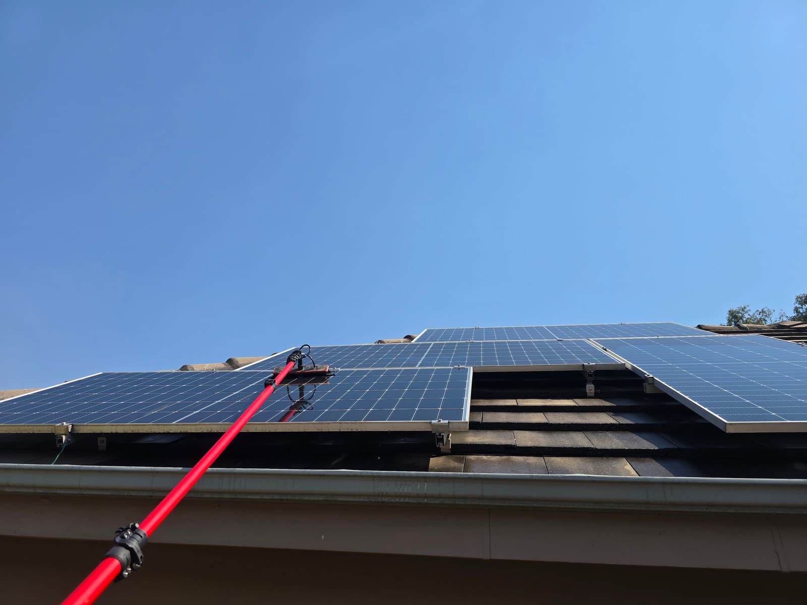 Solar panel cleaning pole in action against a clear blue sky